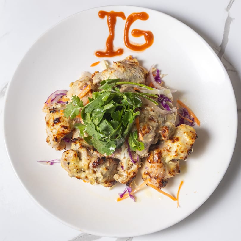 Indian Garden's chicken malai tikka, garnished with cilantro, onions, and carrots, on a white plate.