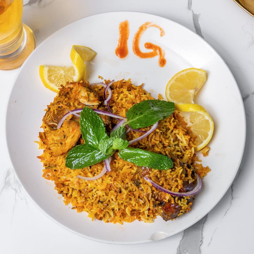 Indian Garden's chicken biryani, garnished with mint, red onions, and lemon wedges, on a white plate.