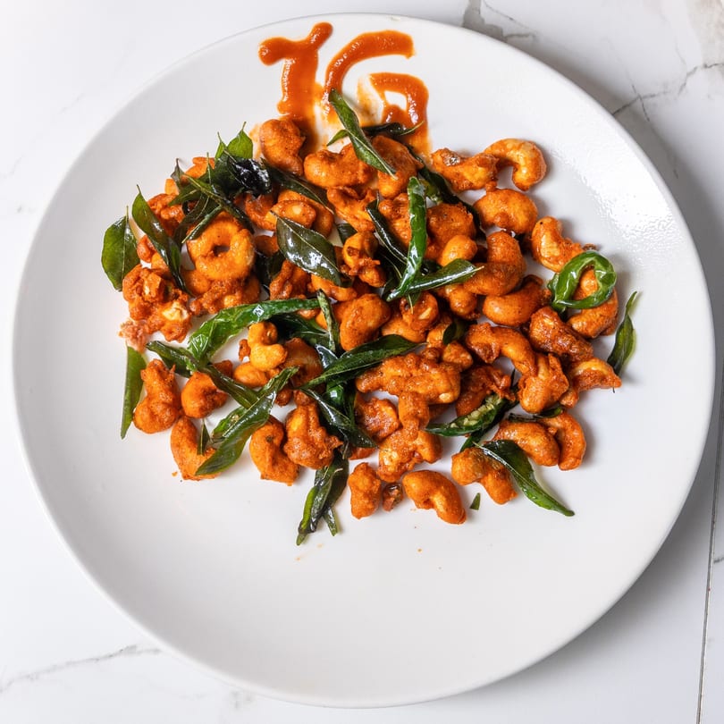 Indian Garden's fried cashews with green leaves and a red sauce drizzle on a white plate.