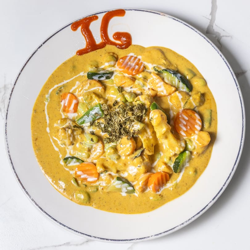 Indian Garden's creamy yellow curry with chicken, carrots, zucchini, and herbs, garnished with "IG" in sauce.