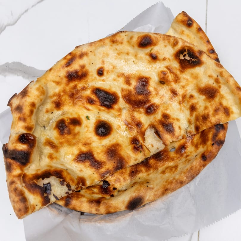 Two pieces of Indian Garden's naan bread, golden brown with charred spots, on white parchment paper.
