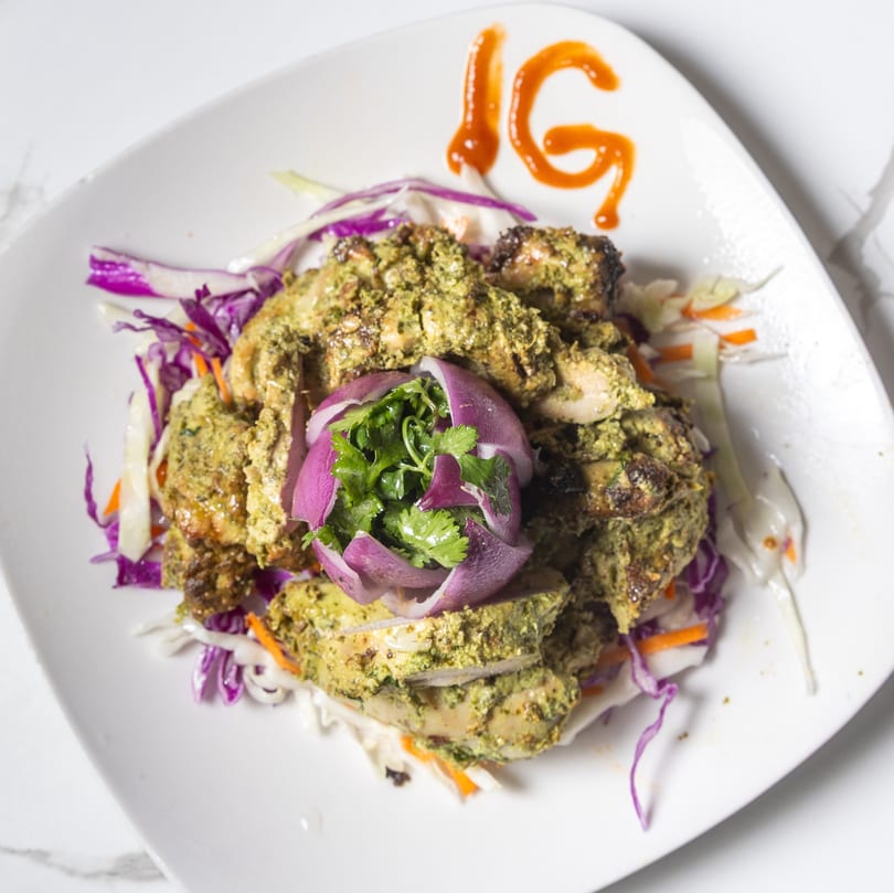 Indian Garden's green-marinated chicken, garnished with red onion and cilantro, on a bed of shredded cabbage.