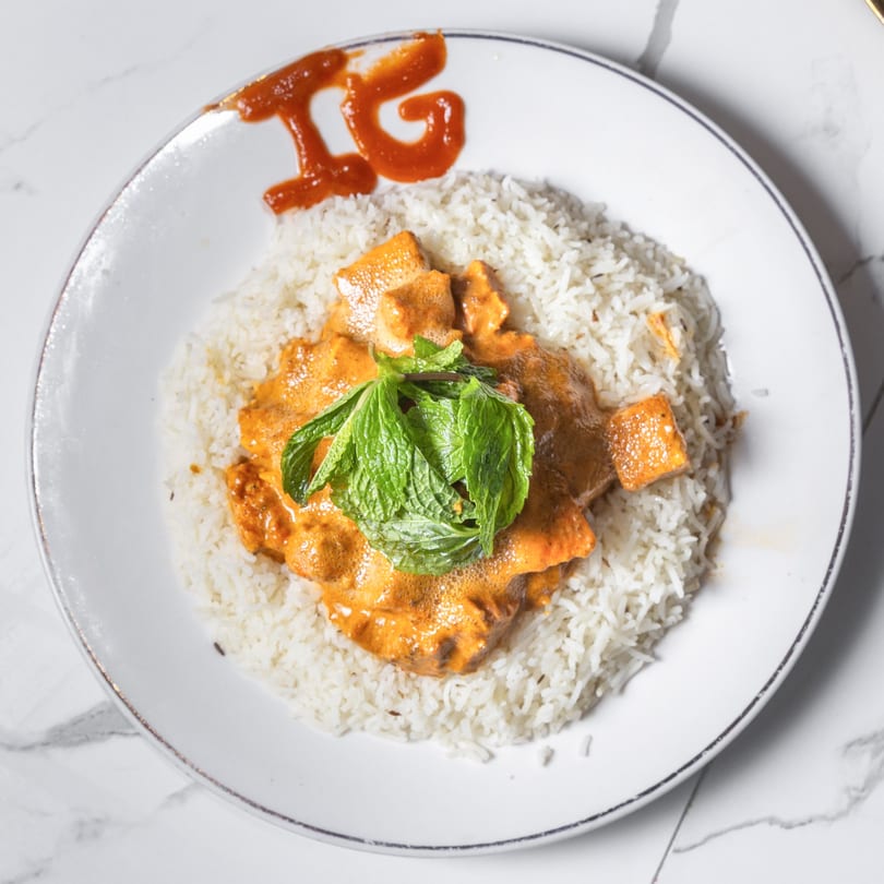 Indian Garden's butter chicken with rice and mint, with "IG" written in sauce on the plate.