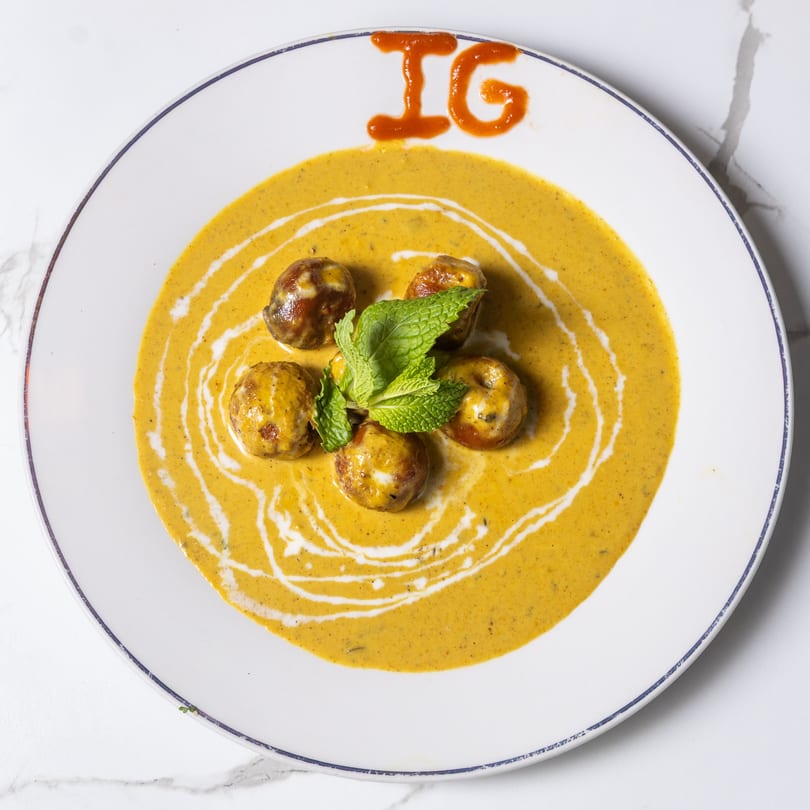 Indian Garden's Indian dish with meatballs in a yellow sauce, garnished with mint and "IG" in red sauce.
